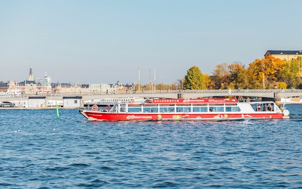 Stockholm sightseeing boat on water near cityscape and bridge.