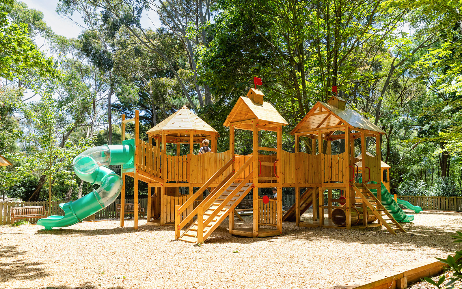 Playhouse with slides at Aschombe Maze & Lavender Gardens, surrounded by trees.