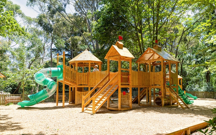 Playhouse with slides at Aschombe Maze & Lavender Gardens, surrounded by trees.