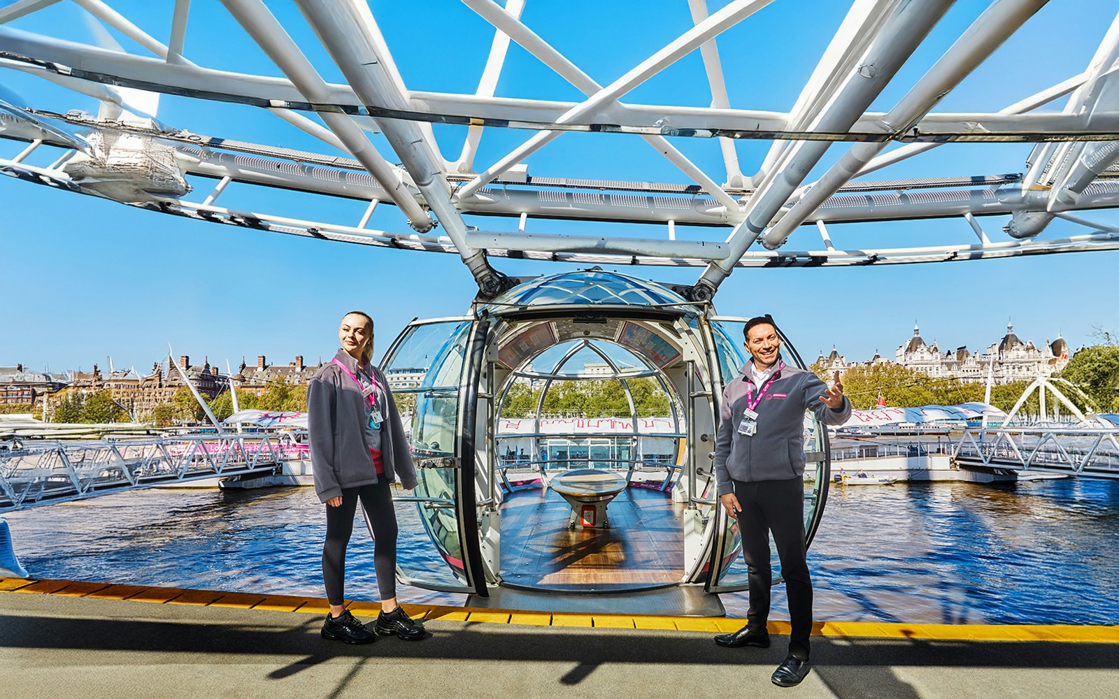 London Eye capsule entrance with staff welcoming visitors, view of Thames River.