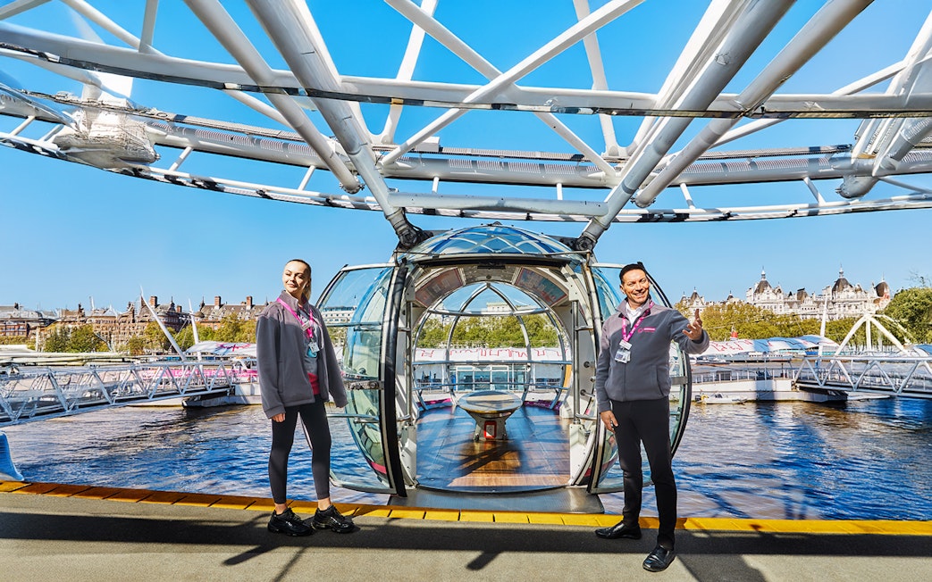 London Eye capsule entrance with staff welcoming visitors, view of Thames River.