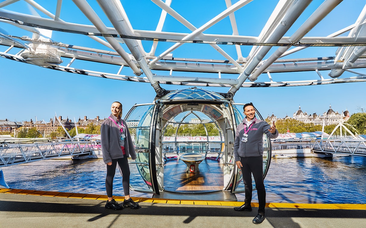 London Eye capsule entrance with staff welcoming visitors, view of Thames River.
