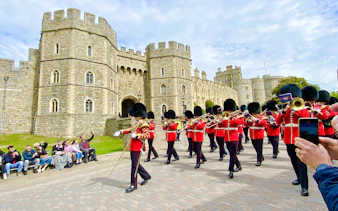 Guards in red uniforms marching at Windsor Castle during the Changing of the Guard ceremony.