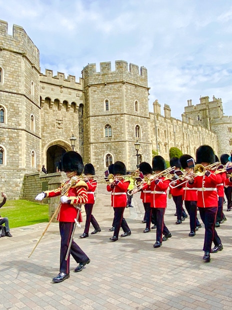 Guards in red uniforms marching at Windsor Castle during the Changing of the Guard ceremony.