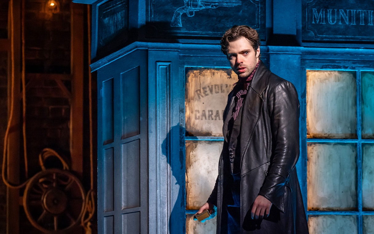 Performer in a dramatic scene from Moulin Rouge! The Musical, standing by a vintage set piece.