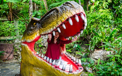 Person inside dinosaur mouth sculpture at Okashigoten Nago Dino Park Yanbaru Subtropical Forest.