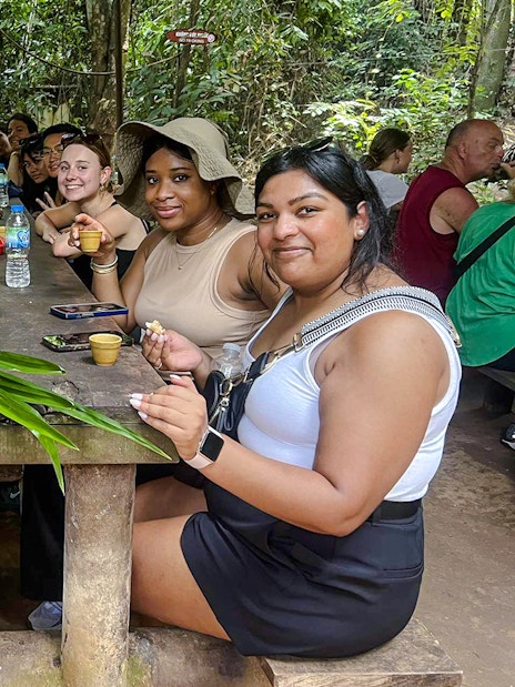 Tour group enjoying snacks at a wooden table in Cu Chi tunnels, Vietnam.