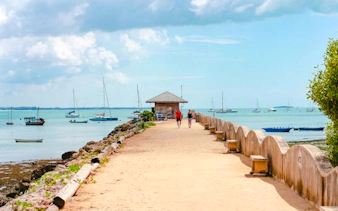 Pier with people walking towards a hut, boats in the water, Dar es Salaam Masaki tour.