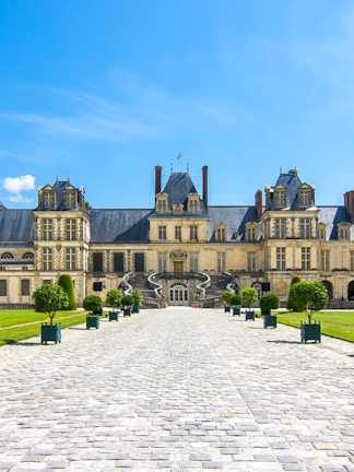 Château de Fontainebleau entrance with cobblestone path and manicured trees.