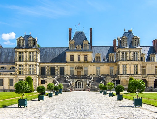 Château de Fontainebleau entrance with cobblestone path and manicured trees.