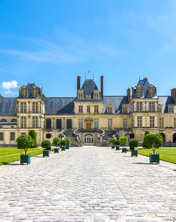 Château de Fontainebleau entrance with cobblestone path and manicured trees.