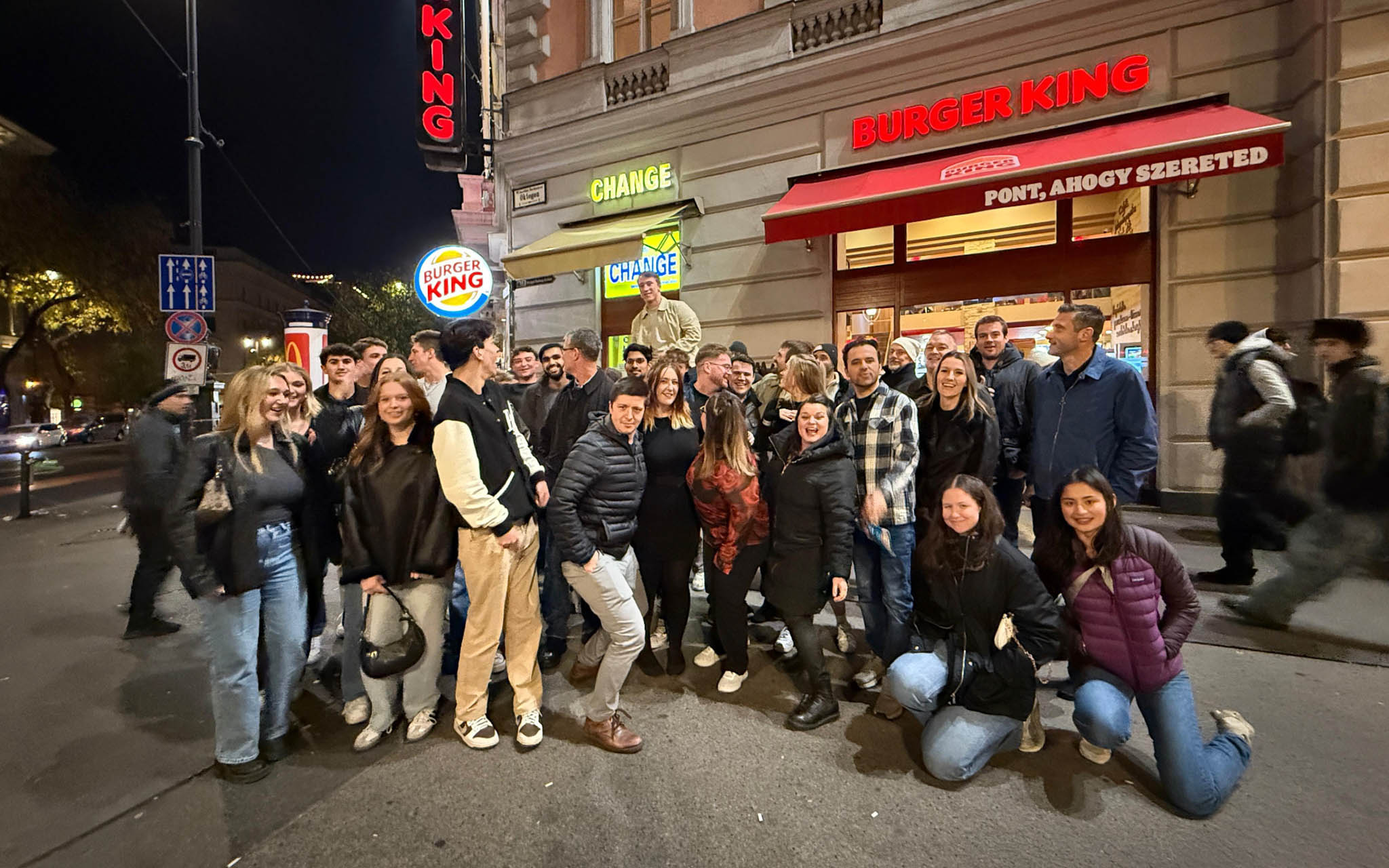 Group of people gathered outside a Burger King during a pub and bar tour at night.