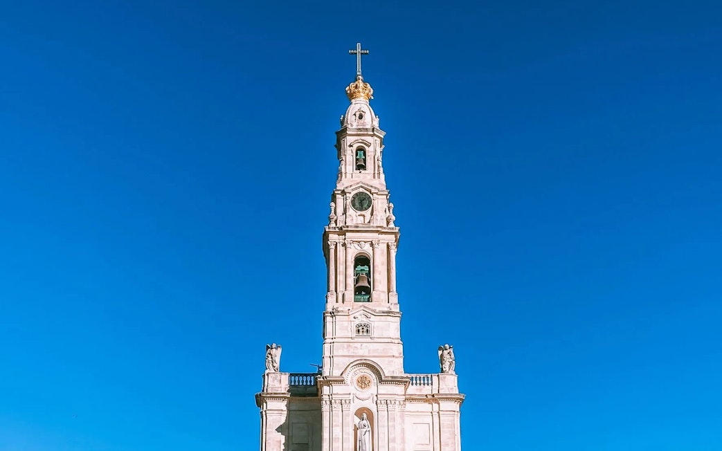 Sanctuary of Our Lady of Fátima bell tower against clear blue sky.