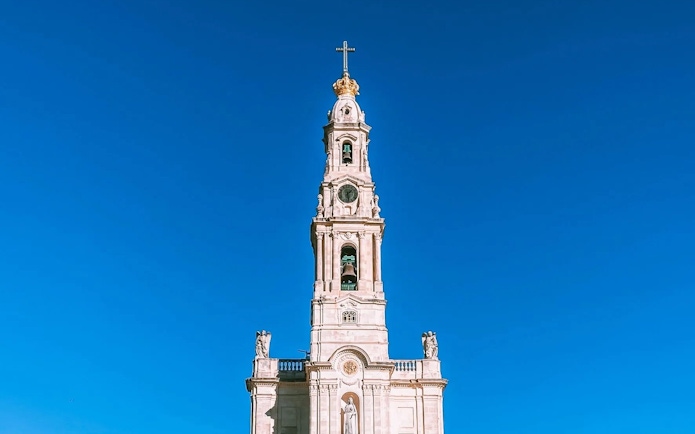 Sanctuary of Our Lady of Fátima bell tower against clear blue sky.
