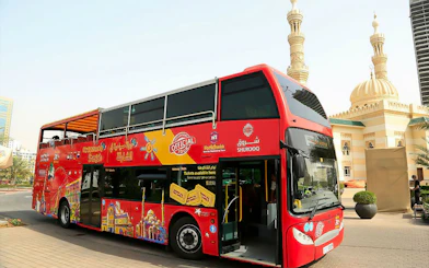 Red double-decker bus for Sharjah Hop-On-Hop-Off Tour near mosque.