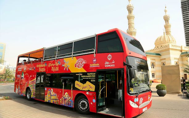 Red double-decker bus for Sharjah Hop-On-Hop-Off Tour near mosque.