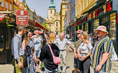Tour group exploring a market street in Prague with historic architecture in the background.