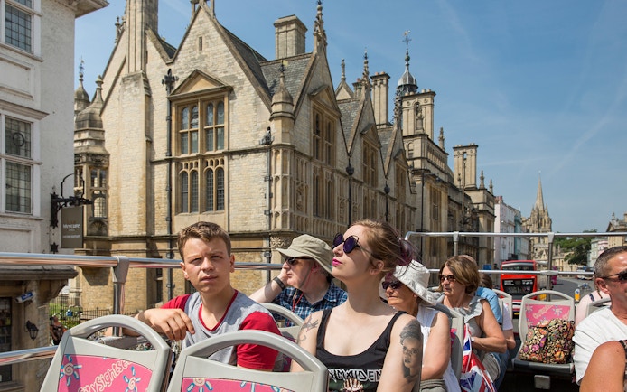 Open-top bus tour passing historic buildings in Oxford.