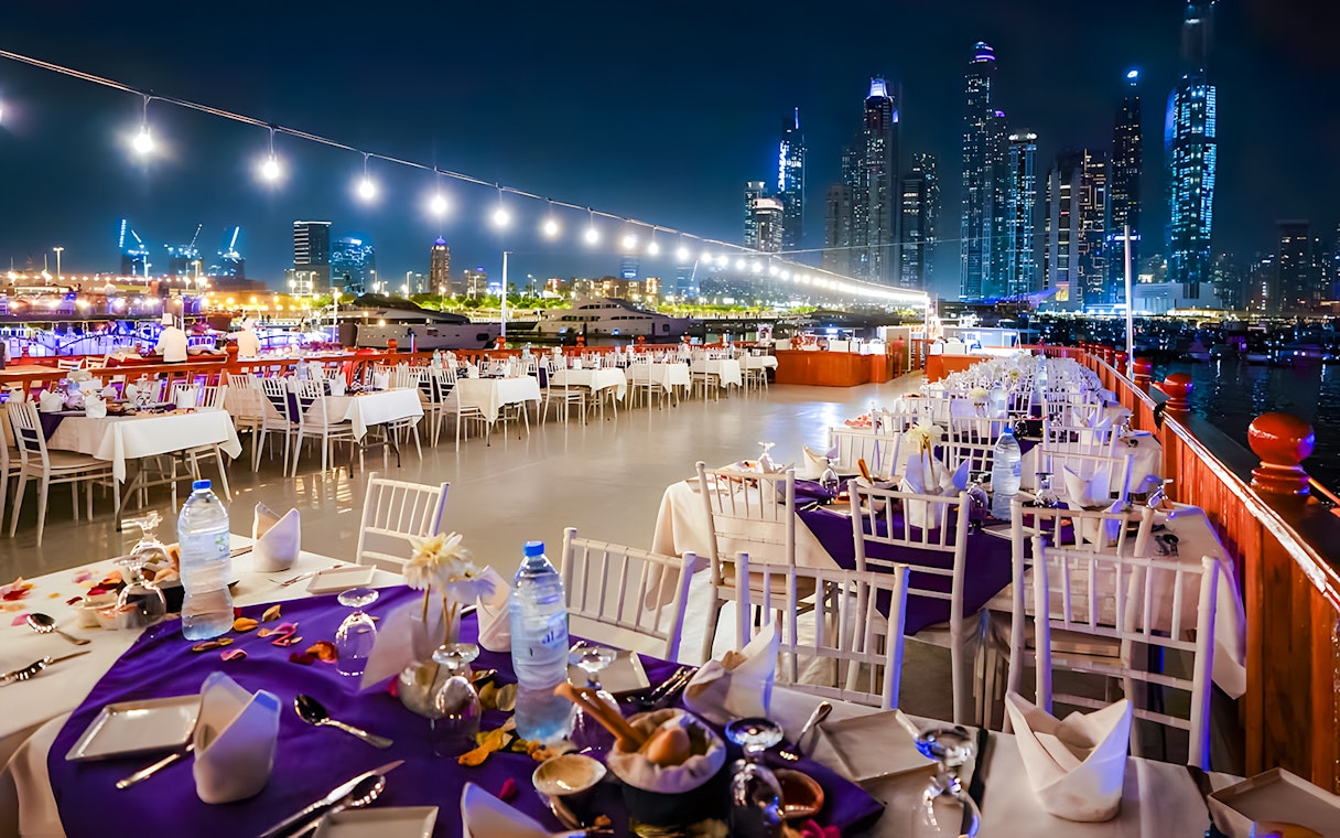 Top deck dining setup on a luxury dhow cruise with Dubai skyline at night.