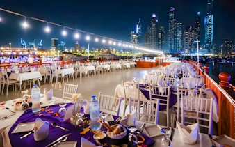 Top deck dining setup on a luxury dhow cruise with Dubai skyline at night.