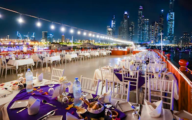 Top deck dining setup on a luxury dhow cruise with Dubai skyline at night.