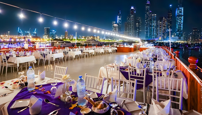 Top deck dining setup on a luxury dhow cruise with Dubai skyline at night.