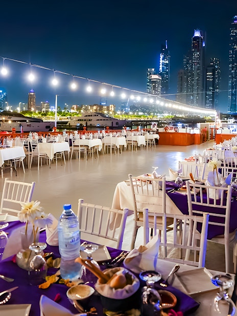 Top deck dining setup on a luxury dhow cruise with Dubai skyline at night.