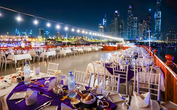Top deck dining setup on a luxury dhow cruise with Dubai skyline at night.