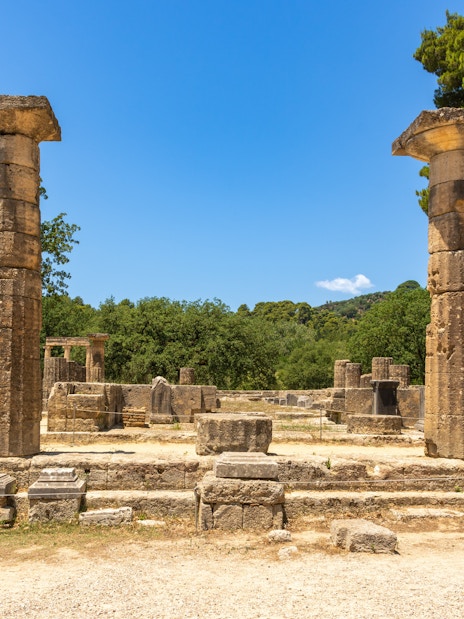 Ancient ruins of the Temple of Hera in Olympia, Greece, with stone columns and trees.