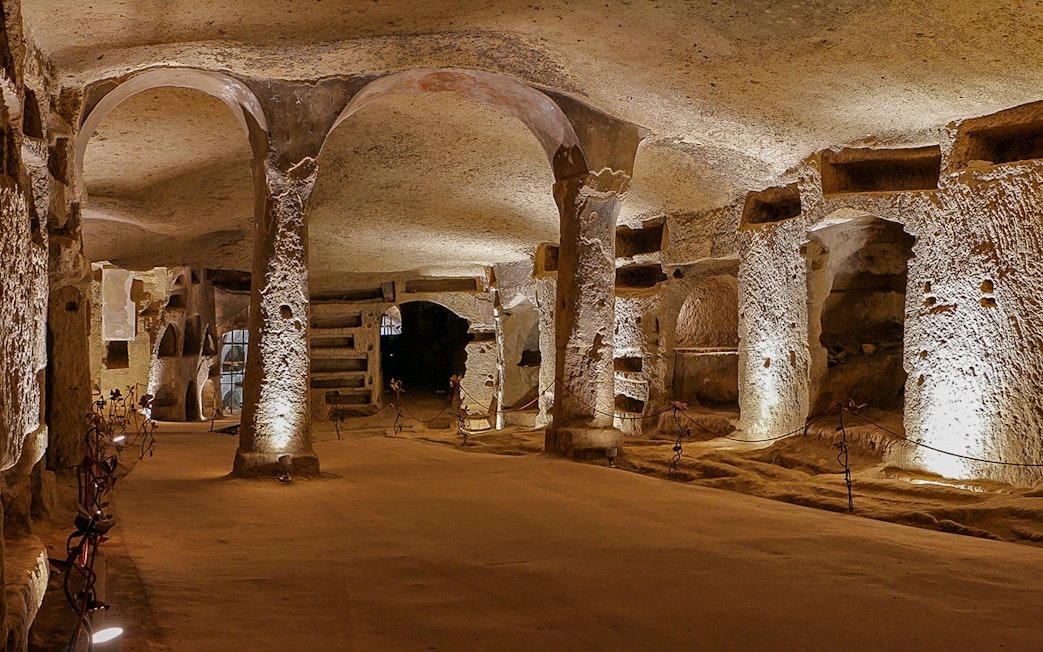 Exploring the ancient Catacombs of San Gennaro in Naples, Italy, with illuminated arches and tombs.