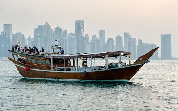 Qatari dhow boat sailing along Doha Corniche with city skyline in the background.