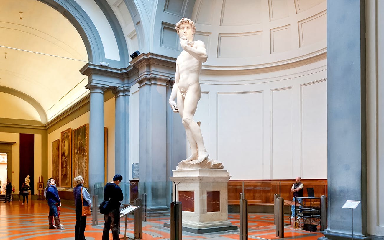 Statue of Michelangelo's David at Accademia Gallery, Florence, with visitors observing.
