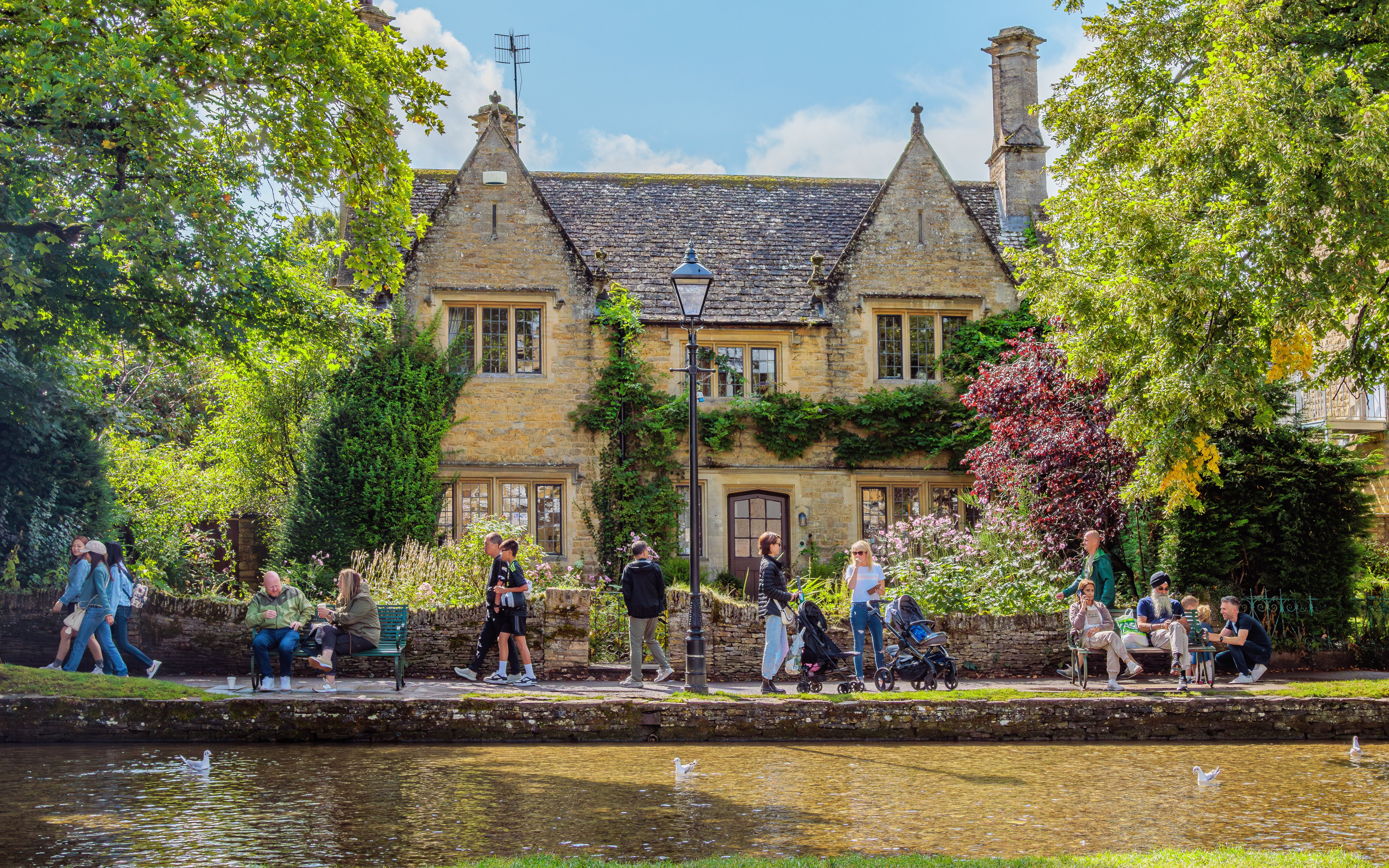 People walking and sitting by a stone house in a Cotswolds village.