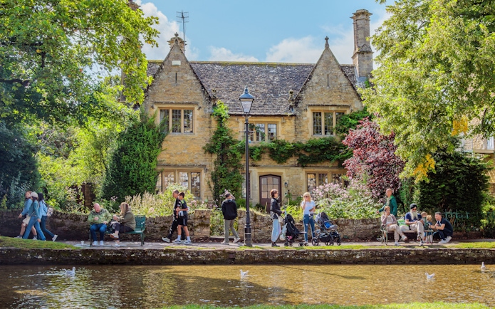 People walking and sitting by a stone house in a Cotswolds village.