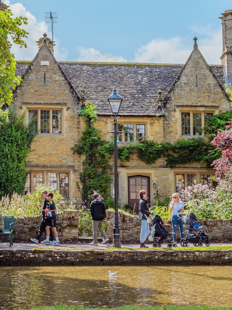 People walking and sitting by a stone house in a Cotswolds village.