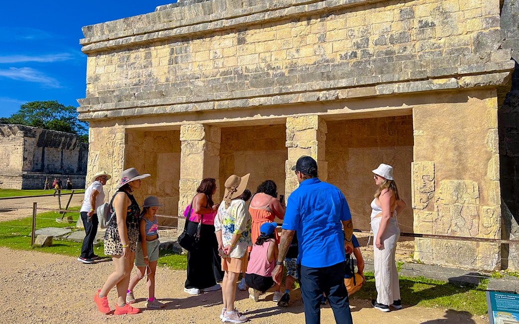 Tourists exploring ancient structures at Chichen Itza during sunrise.
