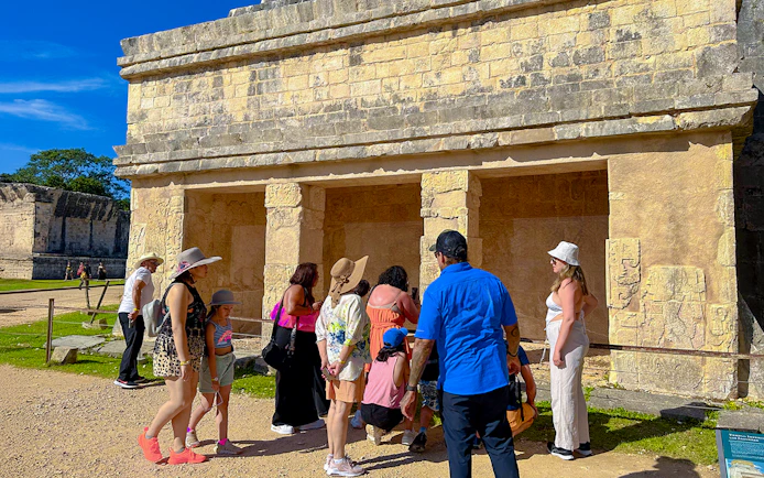 Tourists exploring ancient structures at Chichen Itza during sunrise.