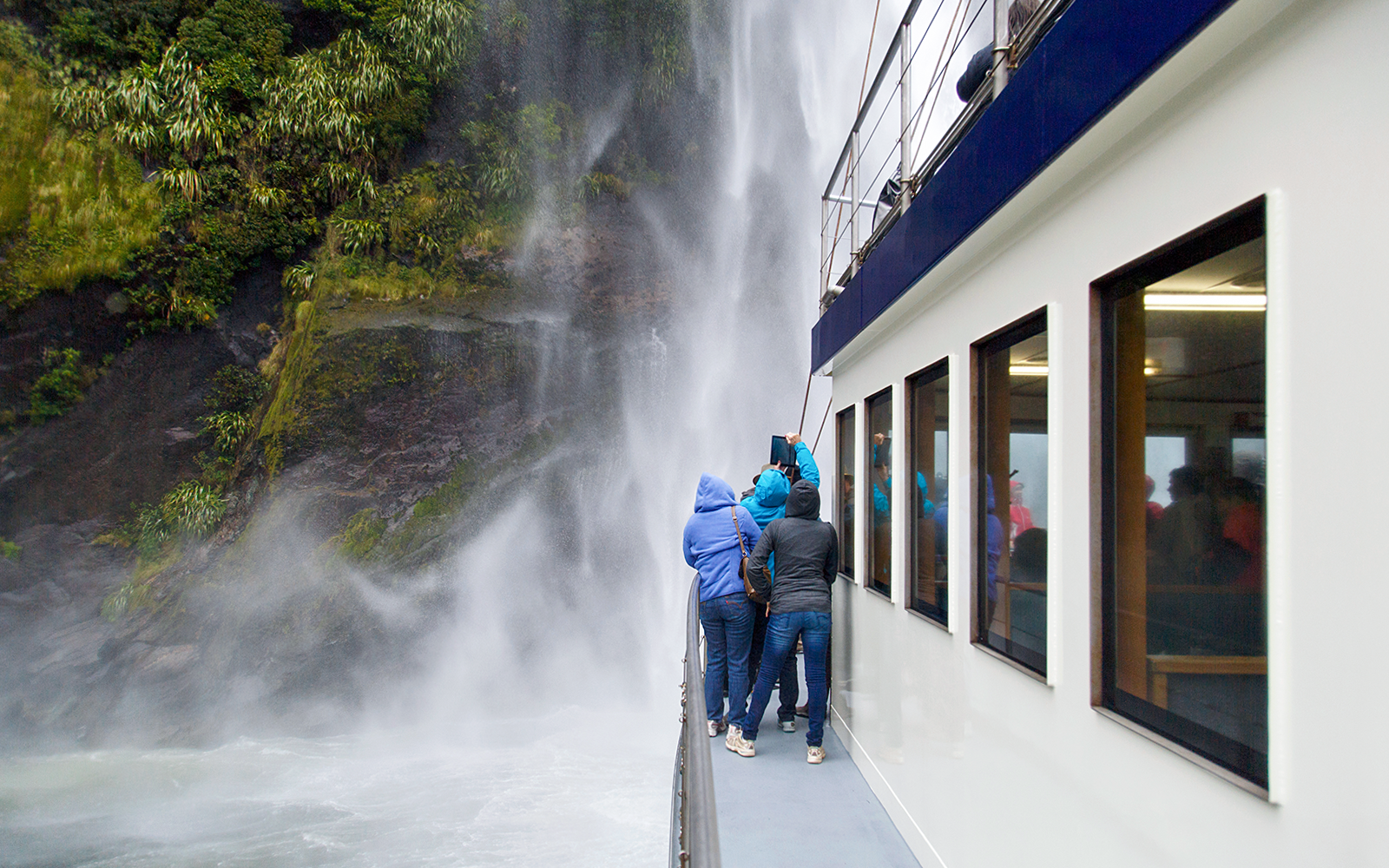 Tourists on a boat viewing a waterfall at Milford Sound, New Zealand.