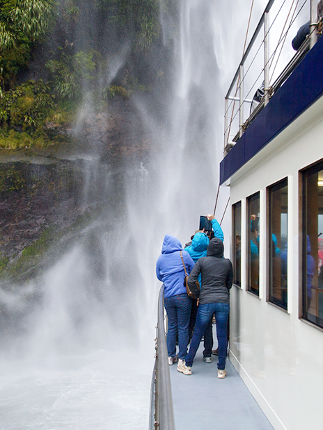Tourists on a boat viewing a waterfall at Milford Sound, New Zealand.