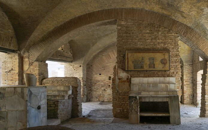 Ancient Roman thermopolium in Ostia Antica with brick arches and frescoes.
