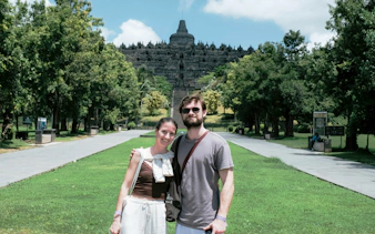 Couple standing in front of Borobudur Temple, Indonesia, surrounded by lush greenery.