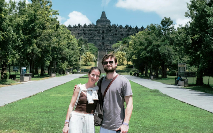 Couple standing in front of Borobudur Temple, Indonesia, surrounded by lush greenery.