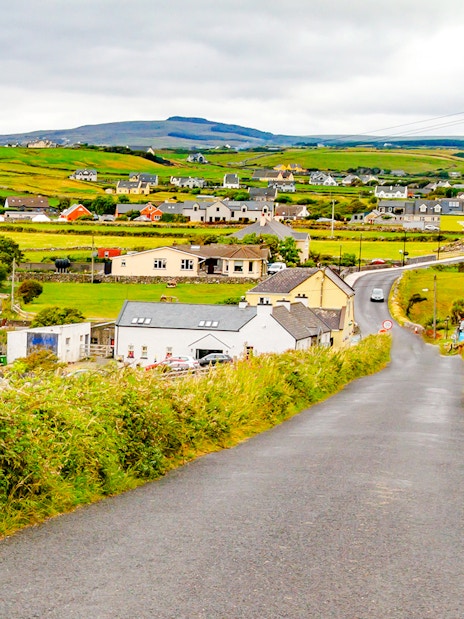 Doolin village road with houses and green fields in County Clare, Ireland.