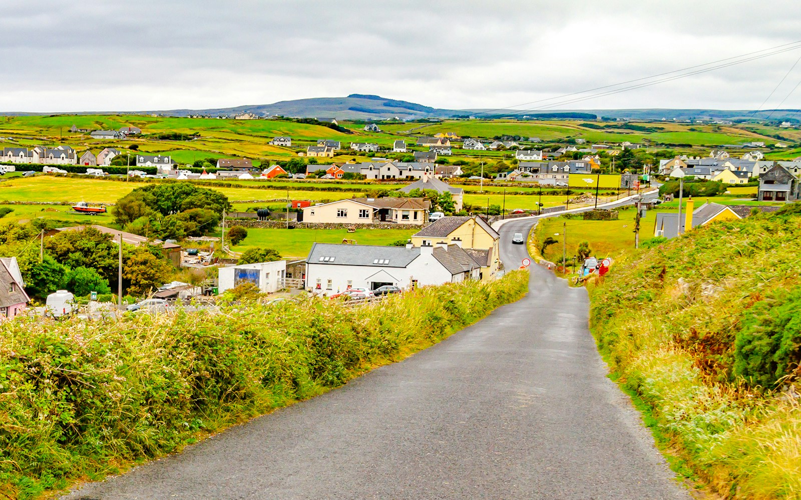 Doolin village road with houses and green fields in County Clare, Ireland.
