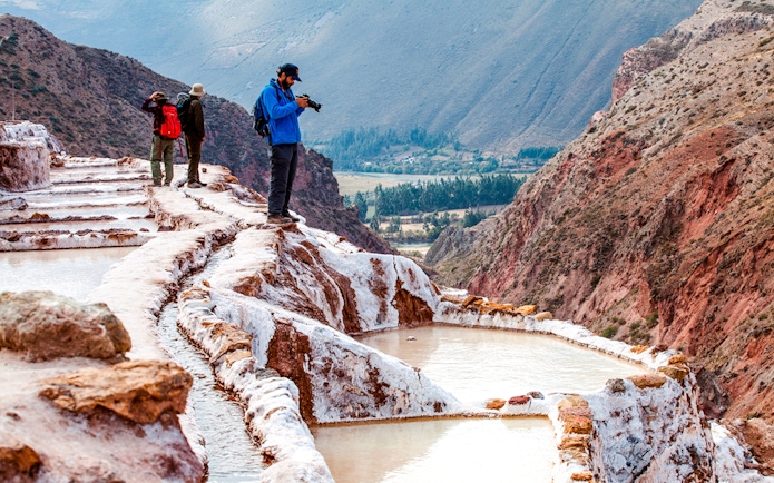 Tourists exploring Maras Salt Mines terraces in Sacred Valley, near Cusco, Peru.