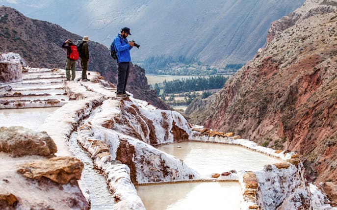 Tourists exploring Maras Salt Mines terraces in Sacred Valley, near Cusco, Peru.