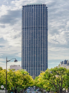Montparnasse Tower in Paris with tree-lined street in foreground.