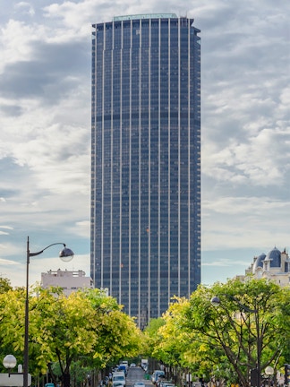 Montparnasse Tower in Paris with tree-lined street in foreground.