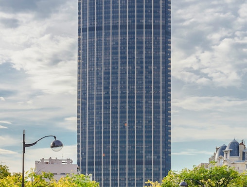 Montparnasse Tower in Paris with tree-lined street in foreground.