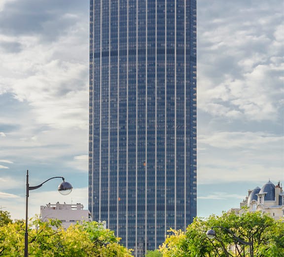 Montparnasse Tower in Paris with tree-lined street in foreground.